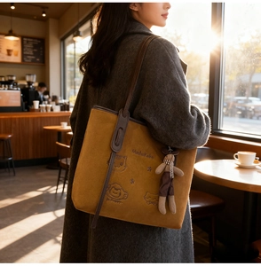 Close-up of brown suede tote bag with cat embroidery and a small bear plush pendant