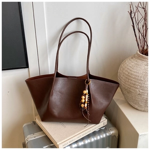 Detail of dark brown matte PU leather tote bag with wooden bead tassel on a suitcase