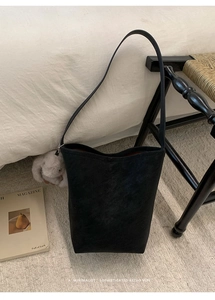 Minimalist black matte leather bucket bag shown in a cozy lifestyle bedroom setting