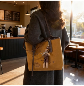 Detail of ginger tote bag featuring cat embroidery, rabbit charm, and leather straps