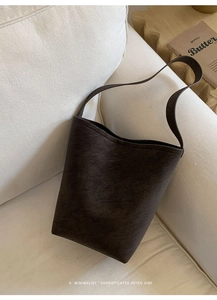 Macro detail of high-quality dark brown suede bucket bag on a minimalist white sofa