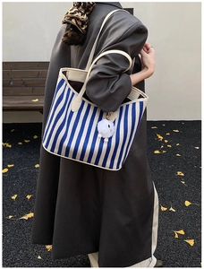 Detail of blue striped canvas tote bag with cream straps and white fuzzy pompom charm