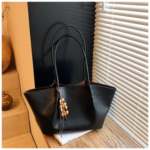 Detail of a large black tote bag with beaded pendant in a natural sunlight setting