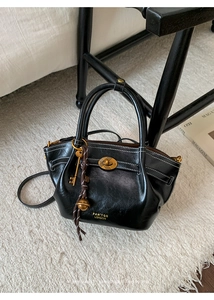 Detail of black leather tote bag with gold logo, contrast stitching, and vintage charms