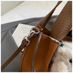Gros plan du sac seau en cuir grainé marron avec boucle argentée et bandoulière amovible