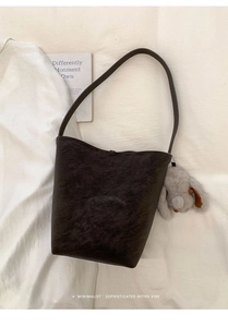 Close-up of retro dark brown bucket bag with a cute plush bunny charm on fabric background
