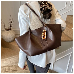 Close-up of vintage brown leather tote bag with colorful ethnic beaded charm detail