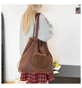Detail of a large brown suede tote bag featuring a round plush fleece accent and drawstring