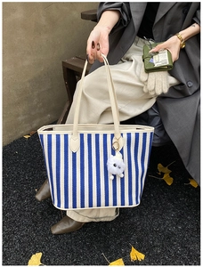 Detail of blue striped canvas tote bag with leather straps and cute monster charm