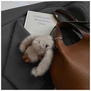 Détail d'un pendentif en peluche beige sur un sac seau en cuir marron avec garniture