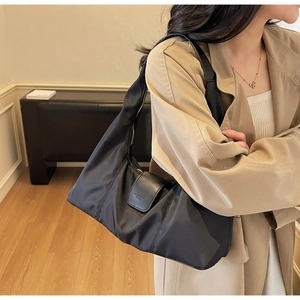 Detailed view of black nylon shoulder bag with leather buckle flap on beige trench coat