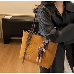 Detail of tan suede tote bag featuring cat embroidery and plush rabbit charm accessory