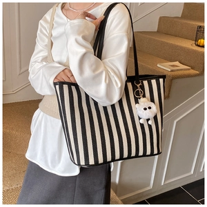Detail of striped canvas tote bag with shoulder strap and a cute white plush doll pendant