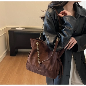 Détail d'un sac cabas en daim marron avec chaînes dorées et cordons de serrage latéraux