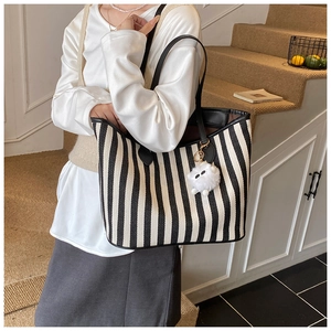 Detail of a large striped canvas tote bag with black leather straps and plush charm