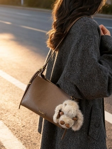 Brown leather shoulder bag with plush bunny charm in warm outdoor sunlight setting