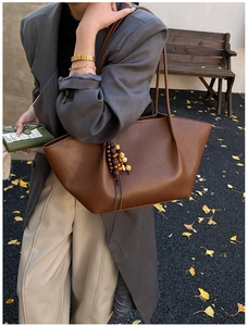 Detailed view of a brown leather tote bag featuring vintage bead charms and long straps