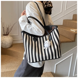 Detail of striped canvas tote bag featuring black leather handles and white pompom charm
