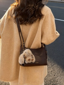 Deep brown leather shoulder bag with plush bunny charm shown on a model at sunset