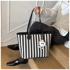 Detailed view of black and white striped canvas tote with plush toy accessory on handle