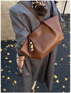 Close-up of brown matte tote bag with vintage wooden bead charm on ginkgo leaves