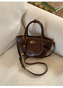 Macro detail of dark brown leather bucket bag with white stitching and gold turn-lock closure