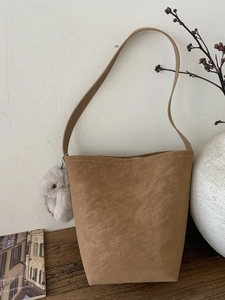 Brown suede bucket shoulder bag with grey plush bunny charm in minimalist lifestyle setting