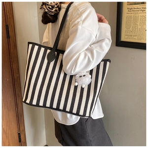 Detail of striped canvas tote bag with black leather straps and white pompom charm