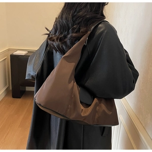 Detailed side view of the brown nylon tote bag shown on a model in a minimal room