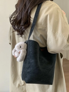 Vintage black matte shoulder bucket bag with plush rabbit charm on trench coat