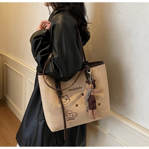 Detail of beige suede tote bag with leather trim and cute bunny plush charm on a model