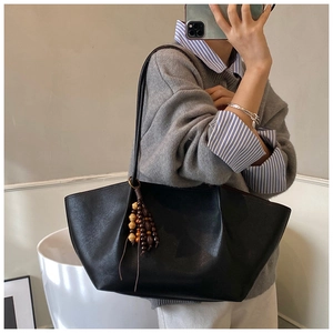 Detail of a black leather tote bag with wooden bead tassel shown in a mirror selfie style