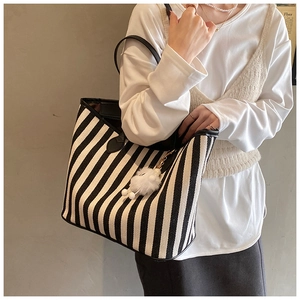 Detail of striped canvas tote bag with black handles and white fuzzy ball charm decoration