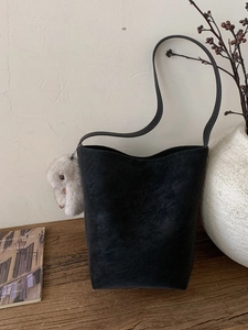 Minimalist black suede bucket bag with a long shoulder strap and cute bunny charm pendant