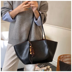 Detail of matte black leather tote bag featuring handcrafted wooden bead tassel accessory
