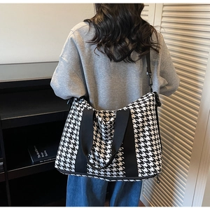Detail of large houndstooth travel bag with adjustable shoulder strap on female model