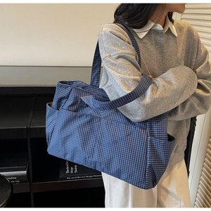 Detailed shot of large blue checkered canvas tote bag with side pockets on model