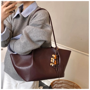 Close-up of vintage dark reddish-brown leather tote bag with unique beaded charm detail