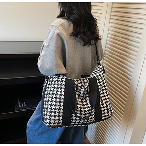 Rear view of a model carrying a large houndstooth travel bag with adjustable straps