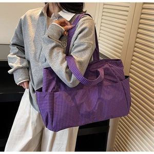 Detail view of purple plaid tote bag with dual straps and side pocket on model