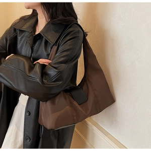 Detail view of large nylon shoulder bag with side leather pocket on minimalist model outfit