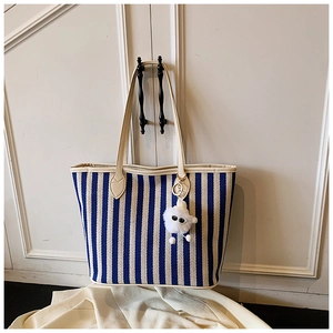 Close-up of blue and white striped canvas tote bag with a cute white plush monster charm