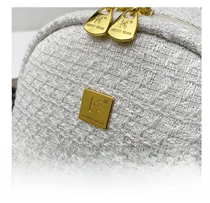 Detail of white tweed fabric texture with gold metal zippers and logo plate on backpack