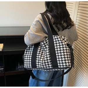 Macro detail of houndstooth travel tote bag with black webbing straps and metal hardware