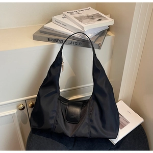 Detailed close-up of a black nylon hobo bag featuring leather straps on a modern chair
