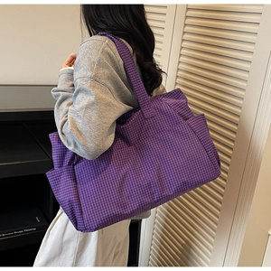 Detail of purple checkered tote bag with side pocket shown on shoulder with casual outfit