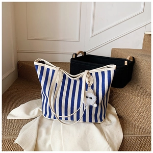Detailed texture of blue striped canvas tote bag with cream leather handle and plush charm