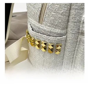 Detail of off-white tweed backpack featuring gold pyramid studs and metal zipper