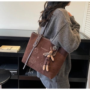Detail of dark brown tote bag with embroidery, rabbit pendant, and leather strap