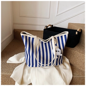 Close-up of blue striped canvas tote bag with plush monster charm and leather handle